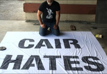 A man sitting on the ground next to a large banner.