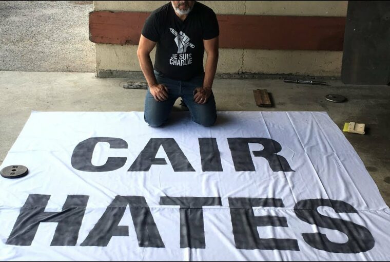 A man sitting on the ground next to a large banner.