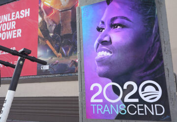 A person walking near a poster of president obama.